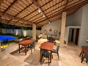 Un patio al aire libre con piscina, mesas y sillas de madera y un muro de ladrillo.