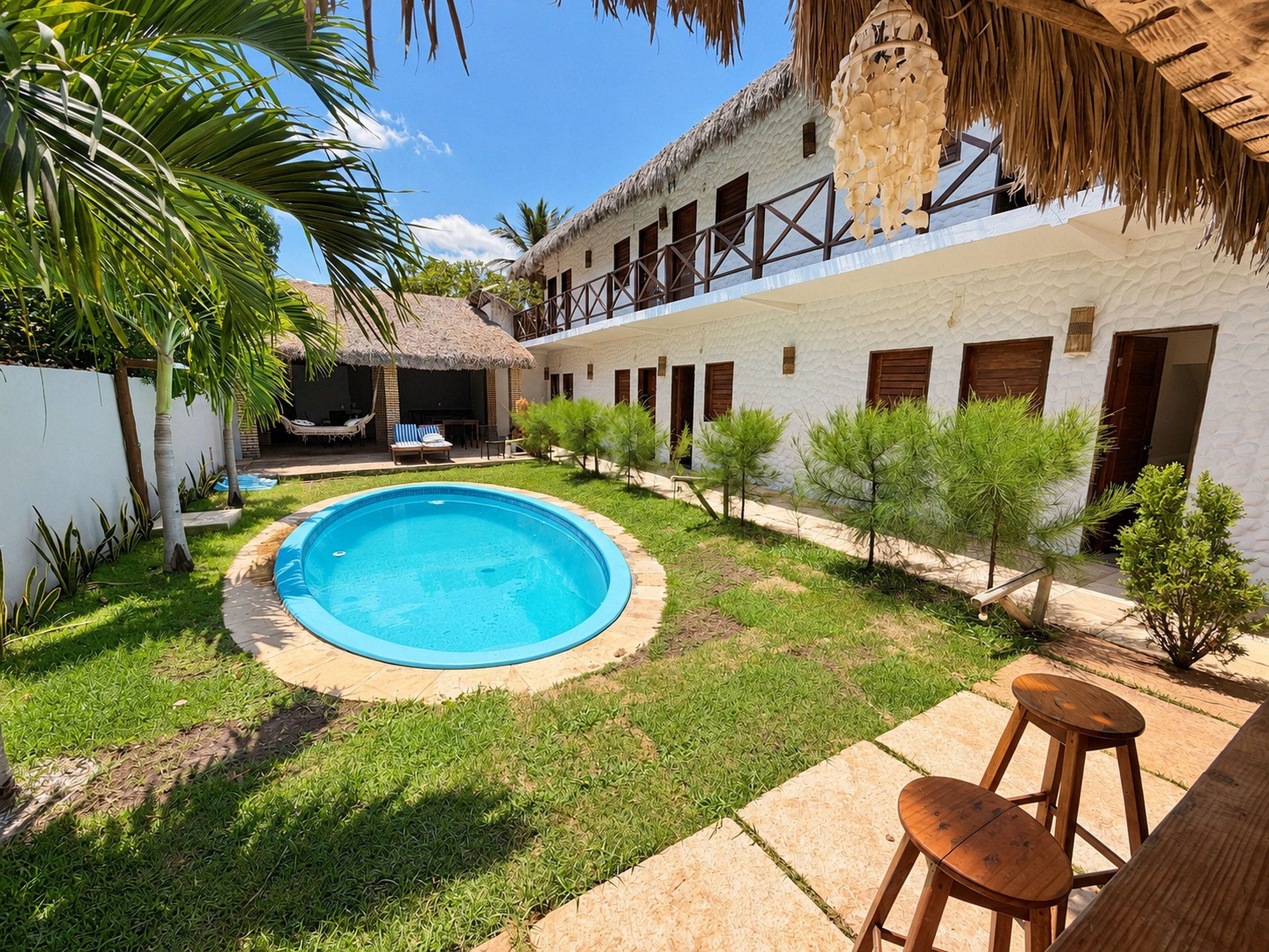 Piscina rodeada por um jardim, com um edifício branco e portas de madeira.