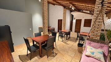 An outdoor dining area with brick pillars, wooden tables, and black woven chairs.