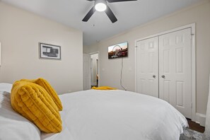 Quarto com uma cama, ventilador de teto, quadro emoldurado e uma porta.