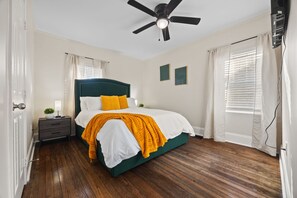 Ein Schlafzimmer mit einem Bett, einem Nachttisch, einem Deckenventilator und einem Fenster mit Jalousien.