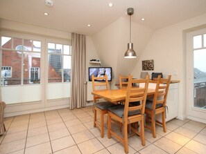 A dining area with a wooden table and chairs, a television on the wall, and a window with curtains. - Rungholtstrasse 6a, Holiday Apartment 3 (Wyk auf Foehr)