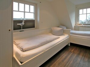 A room with a bunk bed and a single bed, both with white bedding. There is a window with a view of the outside, and a radiator is visible on the wall. - Rungholtstrasse 6a, Holiday Apartment 3 (Wyk auf Foehr)
