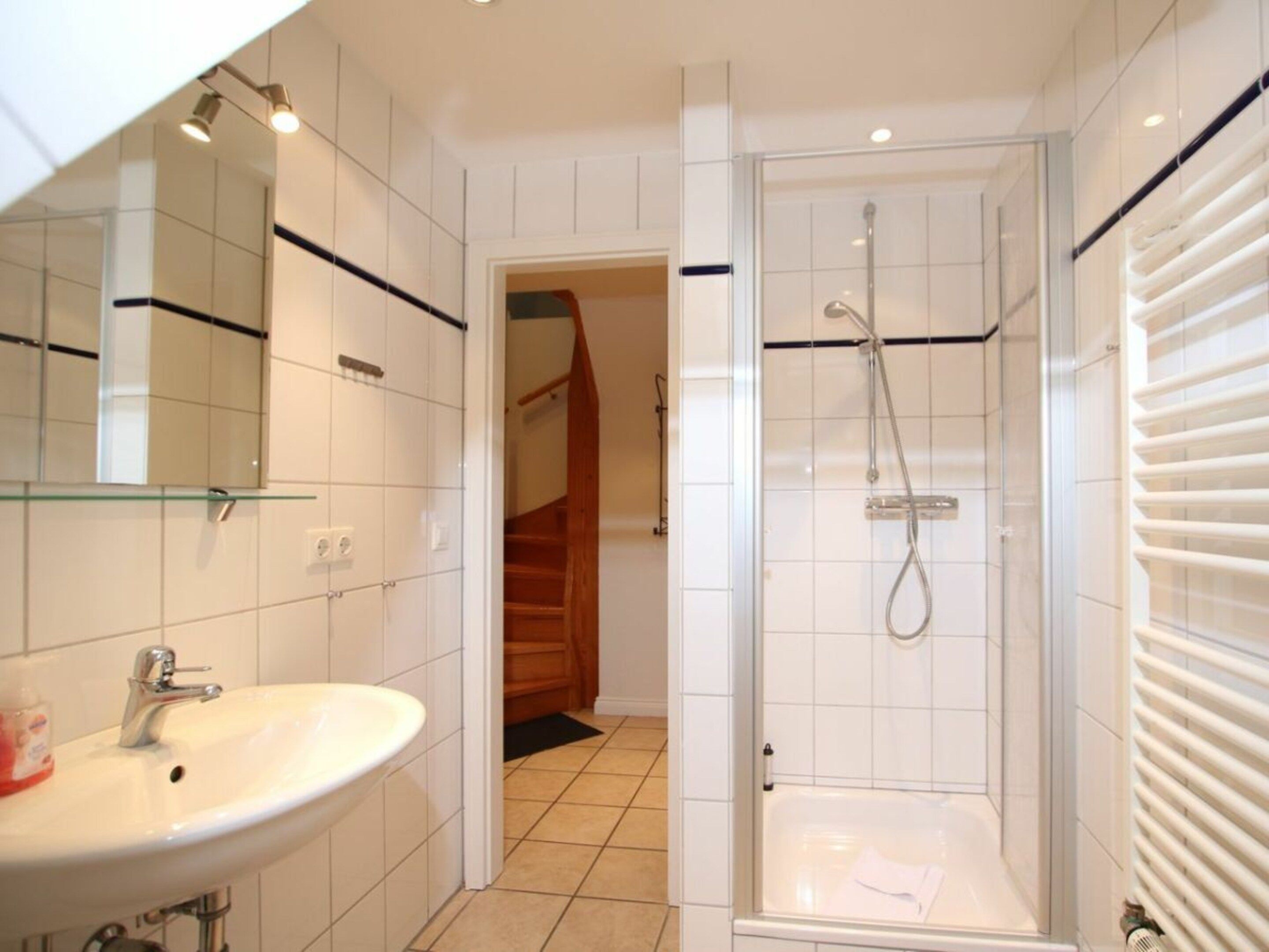 Een badkamer met een wit wastafelmeubel, een douchecabine van glas en een zichtbare trap die naar een andere kamer leidt.