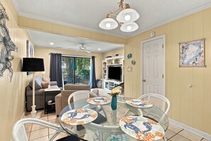 A dining area with a glass table surrounded by chairs, a ceiling fan, and a television on a white entertainment unit. - South Forest Beach Villa Walk to Beach and Coligny (Hilton Head Island)