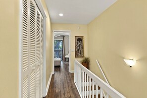 A hallway with a wooden floor, a white railing, and a wall-mounted light fixture. - South Forest Beach Villa Walk to Beach and Coligny (Hilton Head Island)