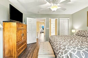 A bedroom with a bed, a wooden dresser, a television, and a ceiling fan. - South Forest Beach Villa Walk to Beach and Coligny (Hilton Head Island)