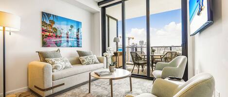 Un salon moderne comprenant un canapé, des fauteuils, une table basse et une grande fenêtre donnant sur la ville.
