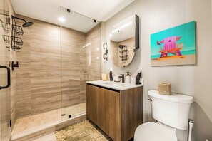 Un baño moderno con ducha envuelta en vidrio, tocador de madera, inodoro y espejo montado en la pared.