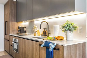 A modern kitchen with wooden cabinets, a built-in oven, a coffee machine, and a sink with a faucet. - Miami Beach Retreat Steps from the Shore (Miami Beach)
