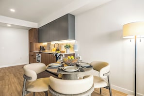 A modern kitchen with a dining area, including a table set for four, a coffee machine, and a fruit bowl. - Miami Beach Retreat Steps from the Shore (Miami Beach)