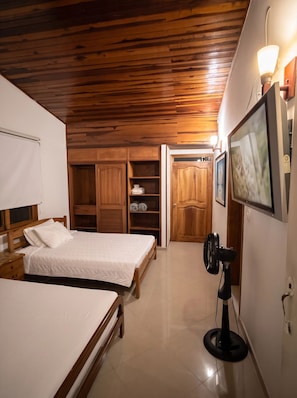 Un dormitorio con dos camas, televisor, ventilador y techo de madera.