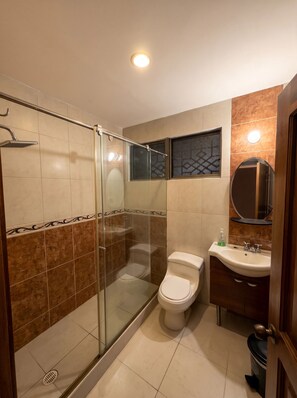 Un baño moderno con cabina de ducha de vidrio, inodoro y lavamanos con espejo.