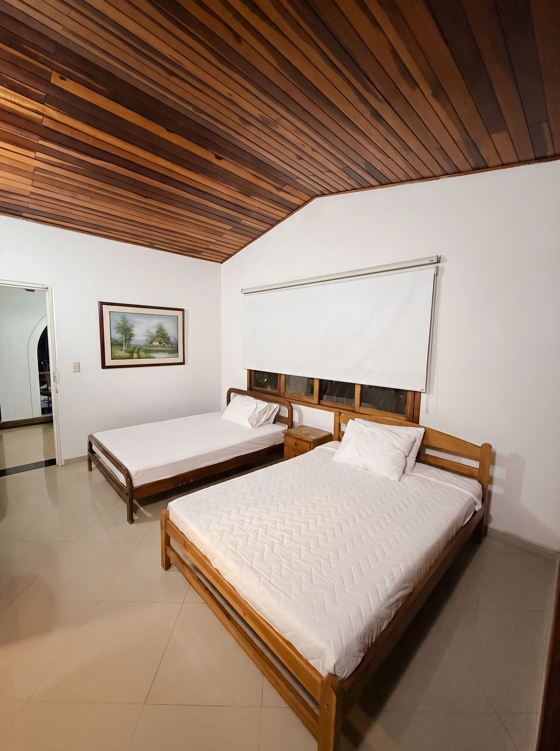 Une pièce avec deux lits en bois, un mur blanc, un tableau encadré et un plafond blanc.