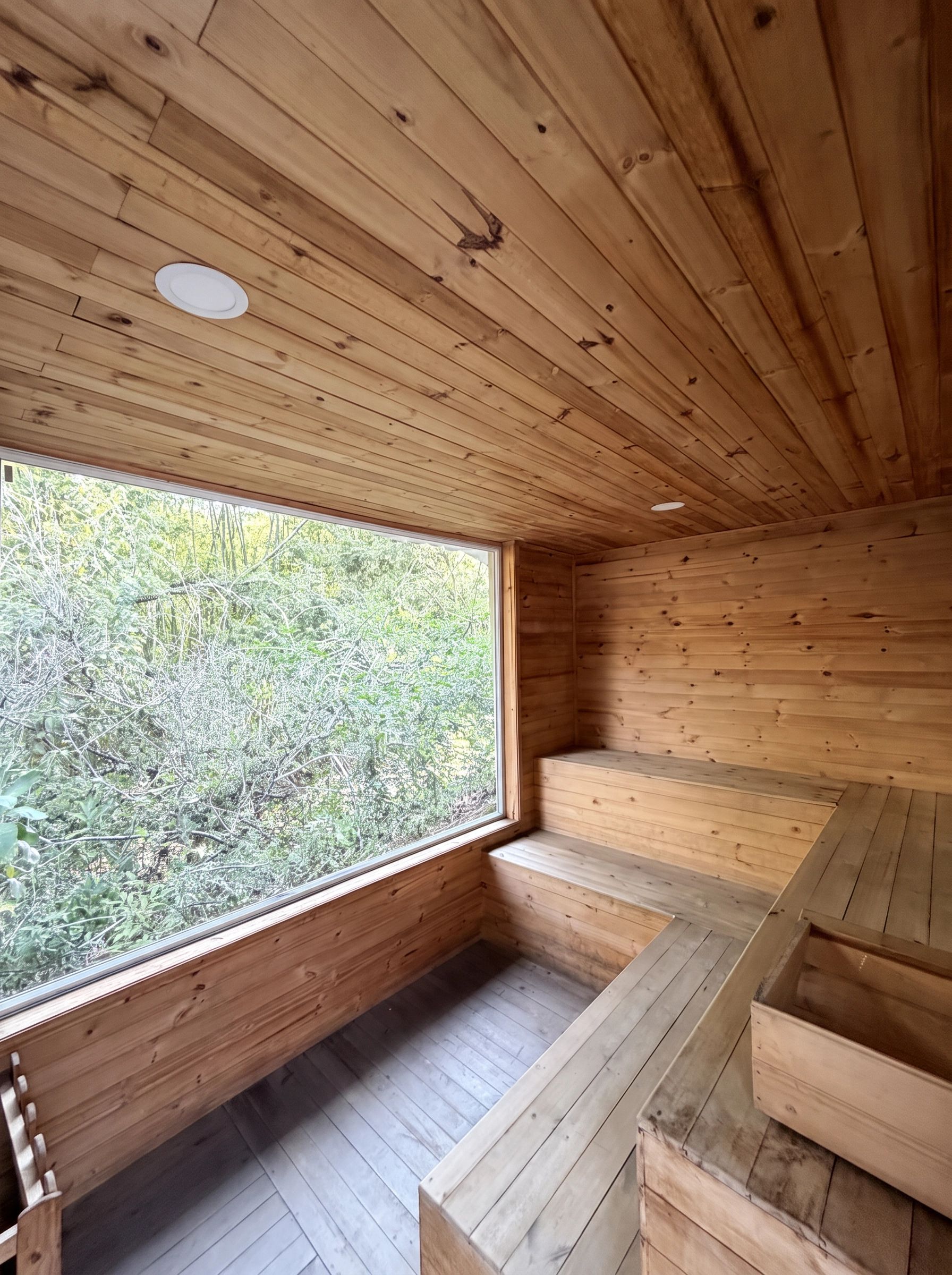 Un interior de madera con un amplio ventanal, suelo de madera y bancos empotrados.