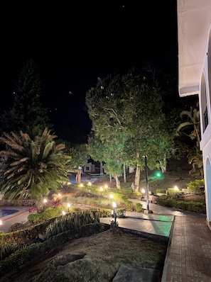 A nighttime outdoor area with a pool, illuminated pathways, and various trees.