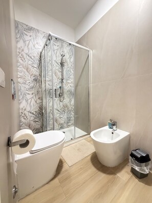 A bathroom with a glass shower enclosure, a toilet, a bidet, and a trash bin. - B&B Int'O'Vico – Deluxe Double Room 6 with Wi-Fi and Air Conditioning (Napoli)