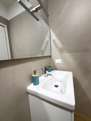 Un baño con un lavamanos blanco, un dispensador de jabón azul y un espejo encima.