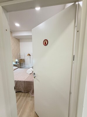 A hotel room with a bed, a towel rack, and a door with a fire safety sign. - B&B Int'O'Vico – Deluxe Double Room 6 with Wi-Fi and Air Conditioning (Napoli)