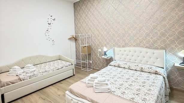 A modern bedroom with two beds, a hanging light fixture, and a patterned wall. - B&B Int'O'Vico – Premium Double Room 29 with Balcony, Wi-Fi & Air Conditioning (Napoli)