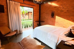 A room with a bed, a chair, a desk, and a view of a garden. - ASA Quinta da Esmeralda Bar Pool Cabins (Itajai)