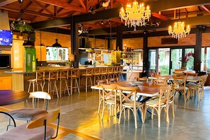 A spacious dining area with wooden tables and chairs, a bar area with stools, and a large chandelier. - ASA Quinta da Esmeralda Bar Pool Cabins (Itajai)