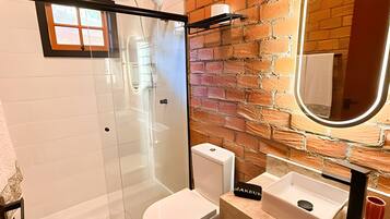 A bathroom with a glass-enclosed shower, a white toilet, a sink with a mirror, and a brick wall.