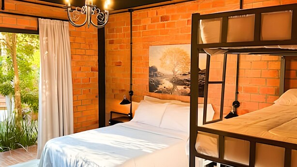 A room with a brick wall, a bed with white bedding, a painting, and a chandelier. - ASA Quinta da Esmeralda Bar Pool Cabins (Itajai)