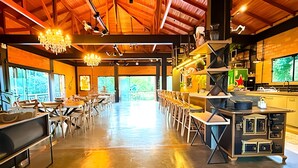 A spacious dining area with high ceilings, exposed beams, and a long counter with stools. - ASA Quinta da Esmeralda Bar Pool Cabins (Itajai)
