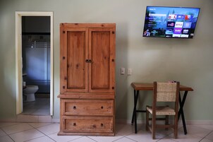 Una habitación con un armario de madera, un televisor montado en la pared y una pequeña mesa con una silla.