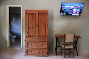 A room with a wooden cabinet, a television mounted on the wall, and a small table with a chair.