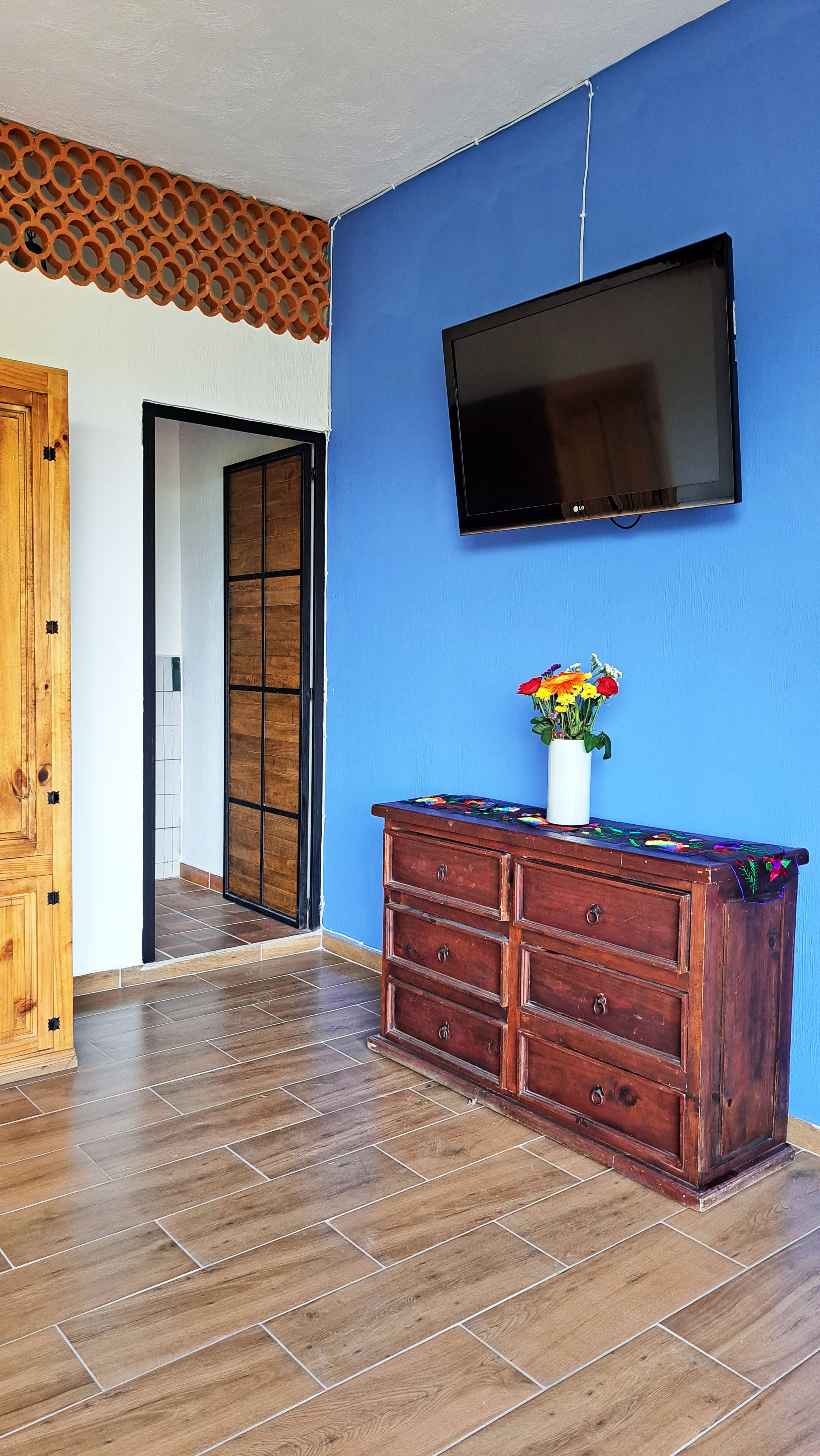 Una habitación con pared azul, un televisor de pantalla plana montado sobre un aparador de madera, y una puerta de madera con diseño decorativo.