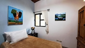 A bedroom with a bed, a window with curtains, a painting of a horse, and a painting of a boat. - Casa Axixic (Chapala)