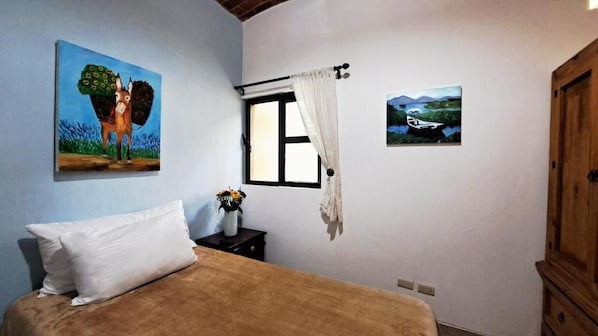 A bedroom with a bed, a window with curtains, a painting of a horse, and a painting of a boat.