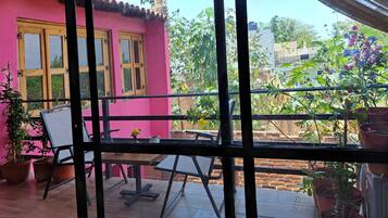 Un balcón con mesa y sillas, plantas en macetas y un edificio rosa con ventanas.