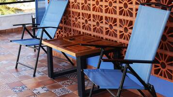A patio with a patterned wall, two blue chairs, and a wooden table.