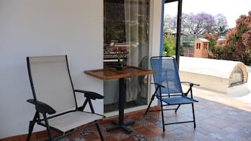 Un espacio de patio con dos sillas, una mesita y vista a un jardín a través de un ventanal.