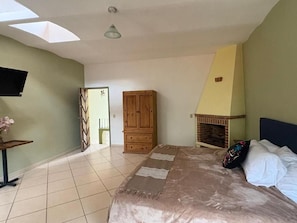 A bedroom with a bed, a television, a wooden wardrobe, a fireplace, and a skylight. - Casa Axixic (Chapala)