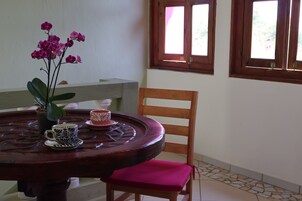Una mesa redonda de madera con un jarrón de flores rosas, dos tazas con diseños y una silla de madera con cojín rosa.