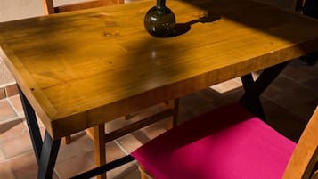 Uma mesa de madeira com um vaso de flores, uma cadeira com almofada rosa e um chão ladrilhado.