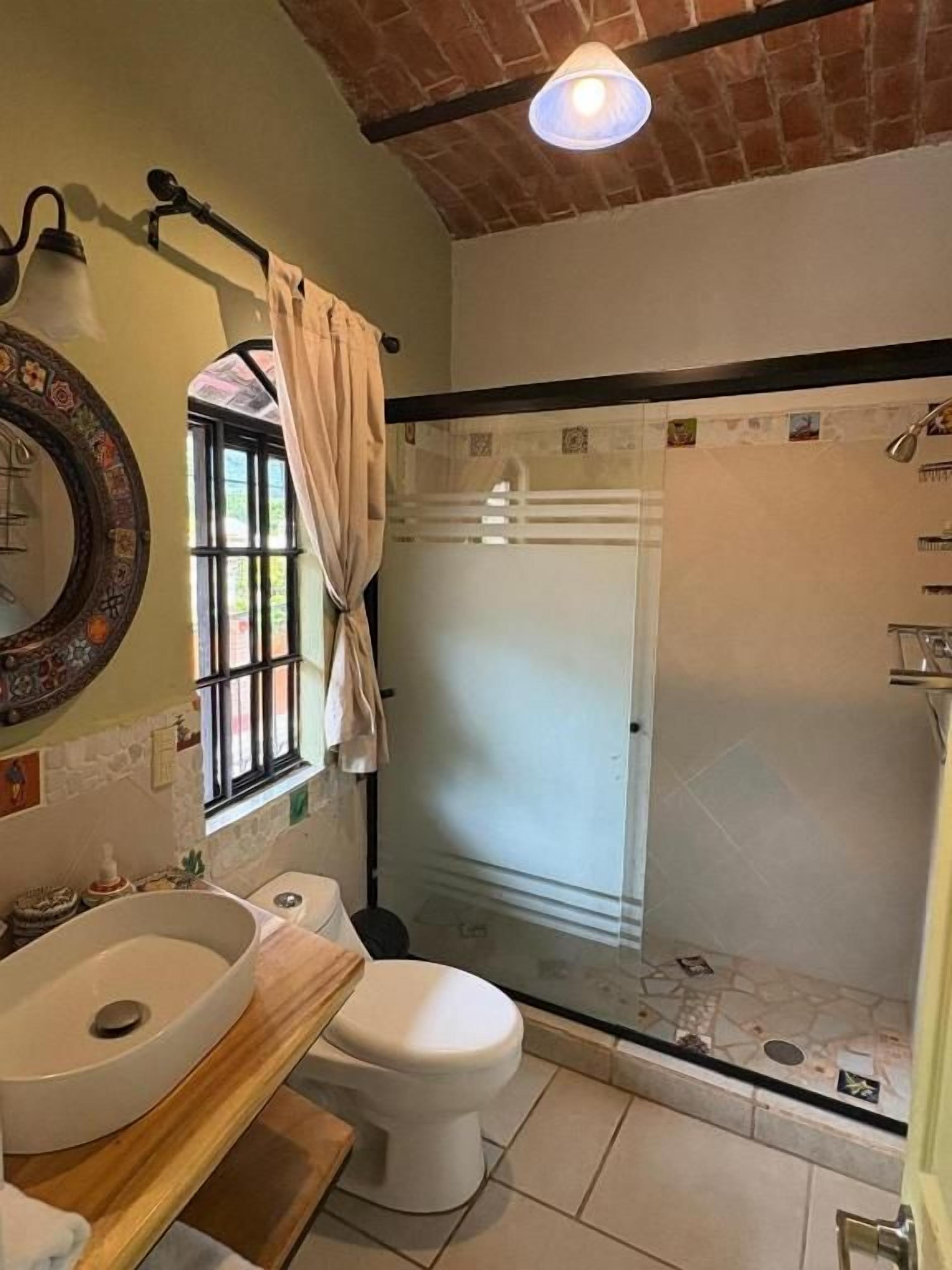 Un baño con un espejo grande, un lavamanos, un inodoro y una zona de ducha con mampara de vidrio.