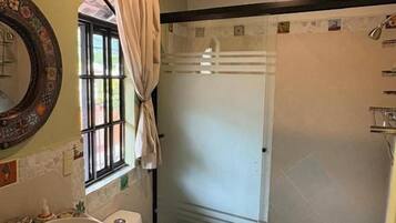 Un baño con un espejo grande, un lavamanos, un inodoro y una zona de ducha con mampara de vidrio.