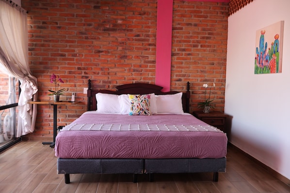 A bedroom with a brick wall, a bed with a purple bedspread, a wooden headboard, and a pink accent wall.