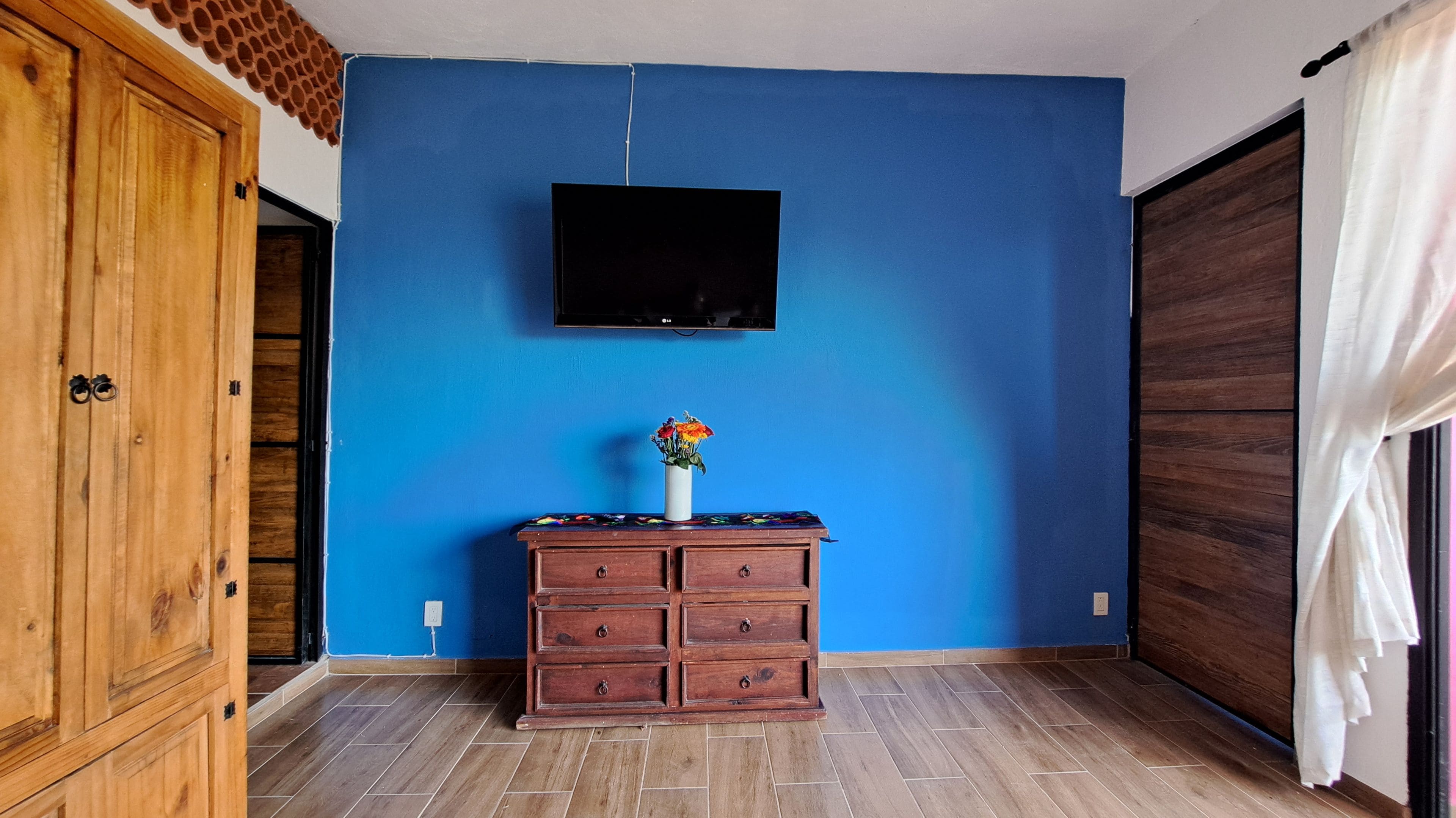 Een kamer met een blauwe wand, een houten kast, een flatscreen televisie en een vaas met bloemen.