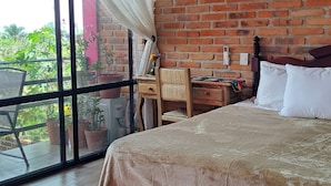 A bedroom with a brick wall, a bed, a desk, and a view of greenery. - Casa Axixic (AJIJIC)