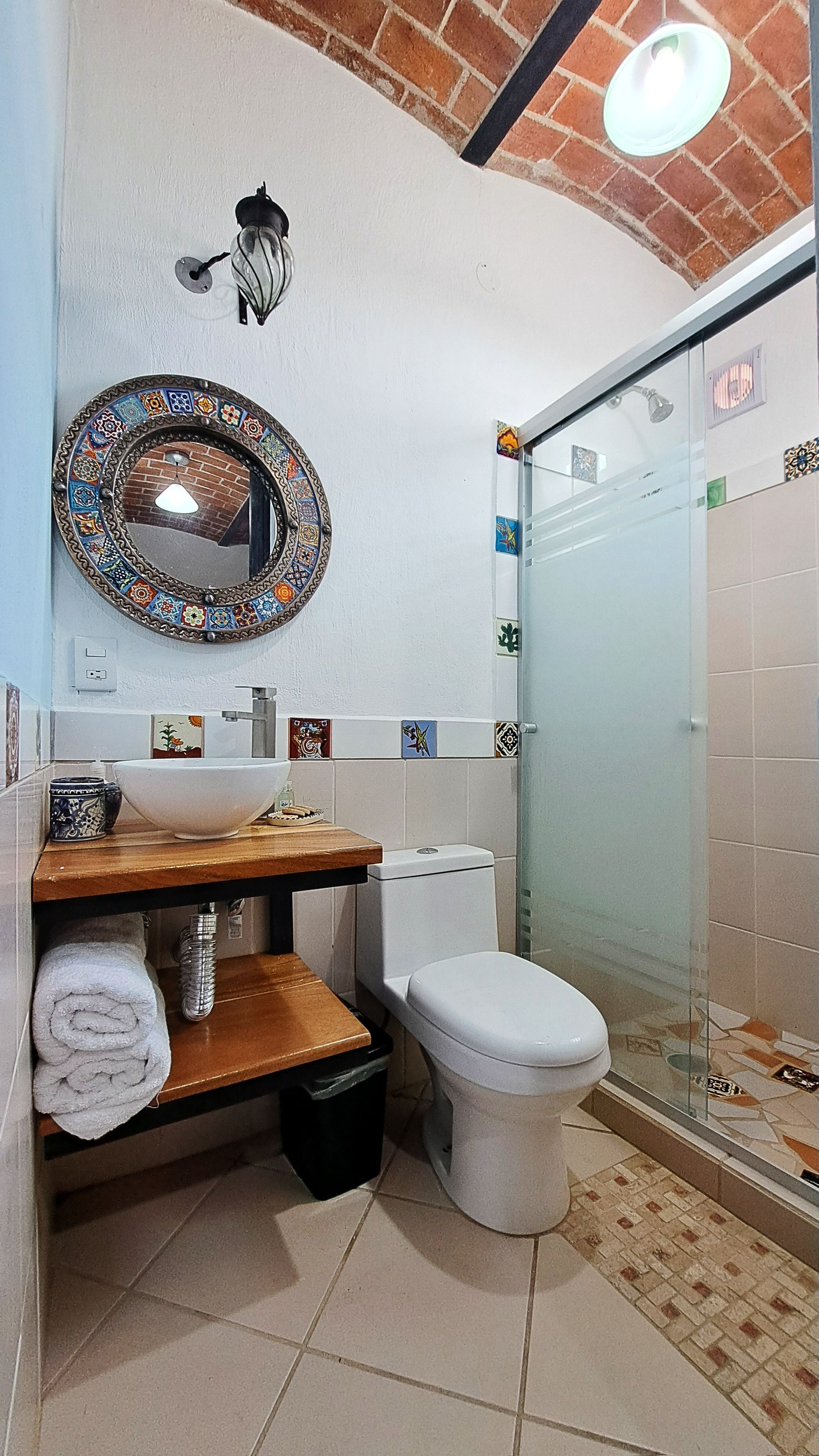 Un baño con un lavamanos blanco, un inodoro, una ducha con puerta de vidrio y un espejo decorativo en la pared.