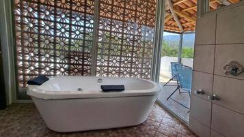 Un baño con una bañera independiente, una puerta de vidrio que da a un espacio exterior y piso de baldosas.