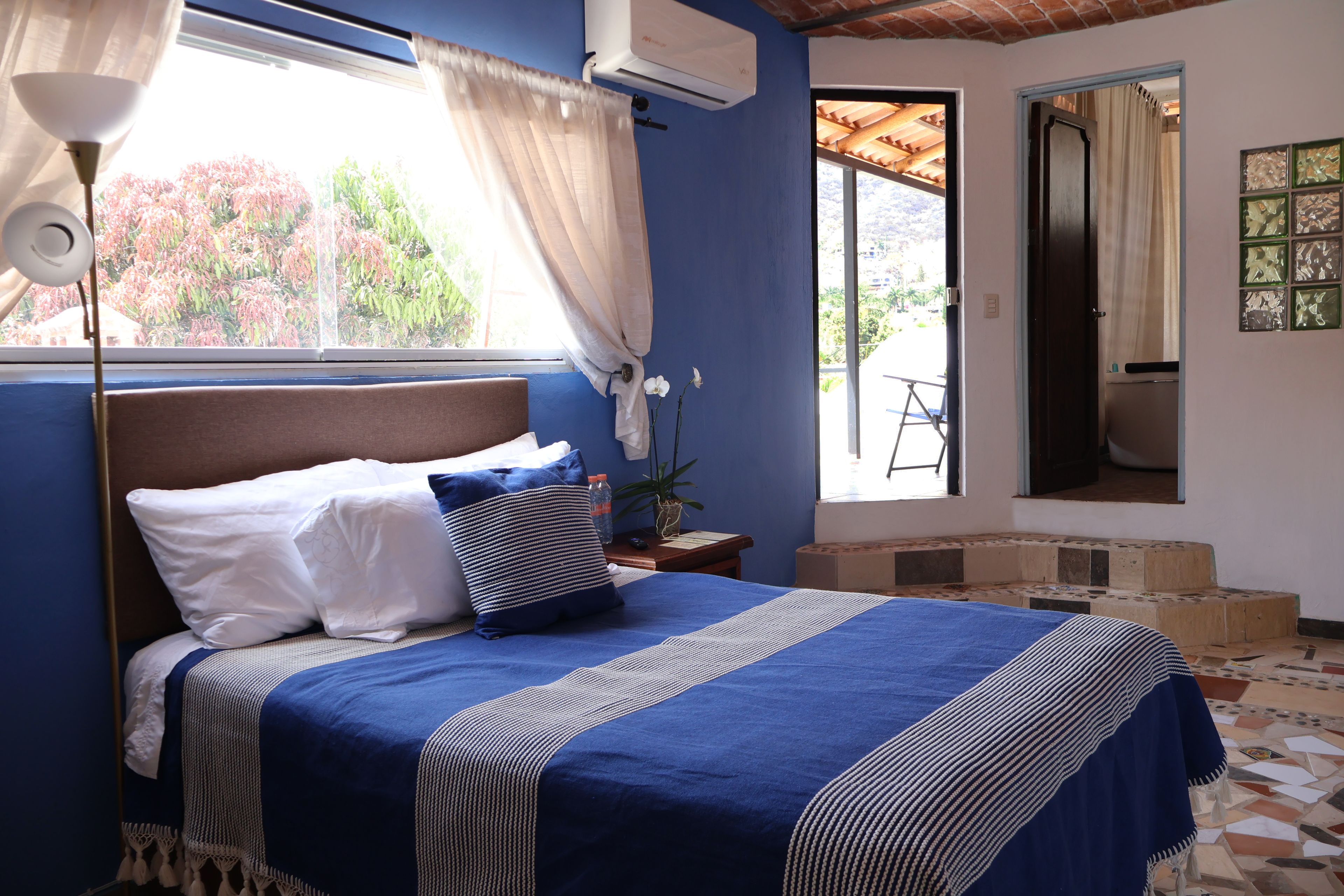 Un dormitorio con cama, ventana con cortinas, equipo de aire acondicionado y vistas al exterior.