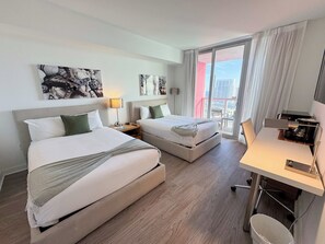 A hotel room with two beds, a desk, and a view of the city. - Beachwalk 2BR Condo| Resort Style with Sunset View (Hallandale Beach)