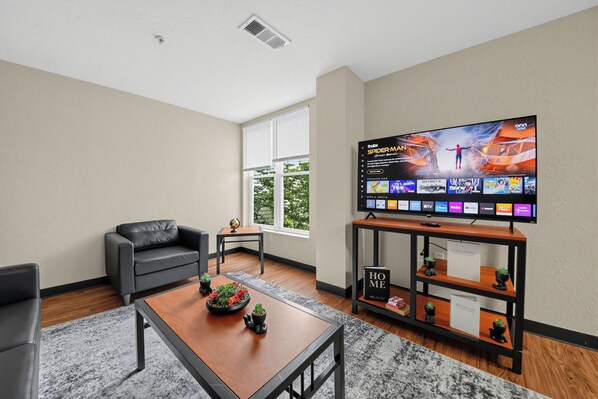 A modern living room with a flat-screen TV, a leather sofa, a coffee table with decorative items, and a bookshelf. - Spacious 4BR, 2BA Home. Mins to UC Med, Zoo & OTR (Cincinnati)